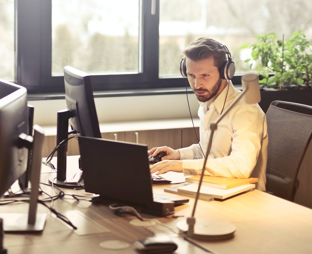 Hombre trabajando con audífonos frente a su computadora